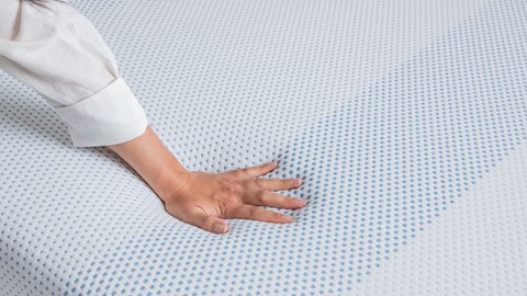 Hand duwt op matras met traagschuim toplaag